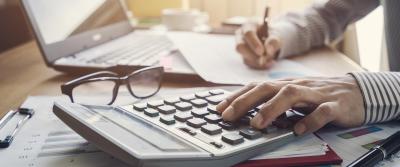 person typing on calculator next to computer